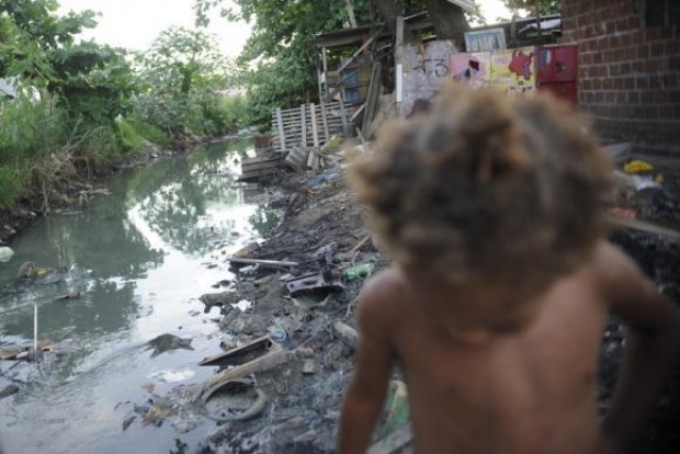 Imagem de riacho e uma criança passando em favela do Complexo da Maré